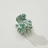 Green and white polka dot hair scrunchie on a light gray background