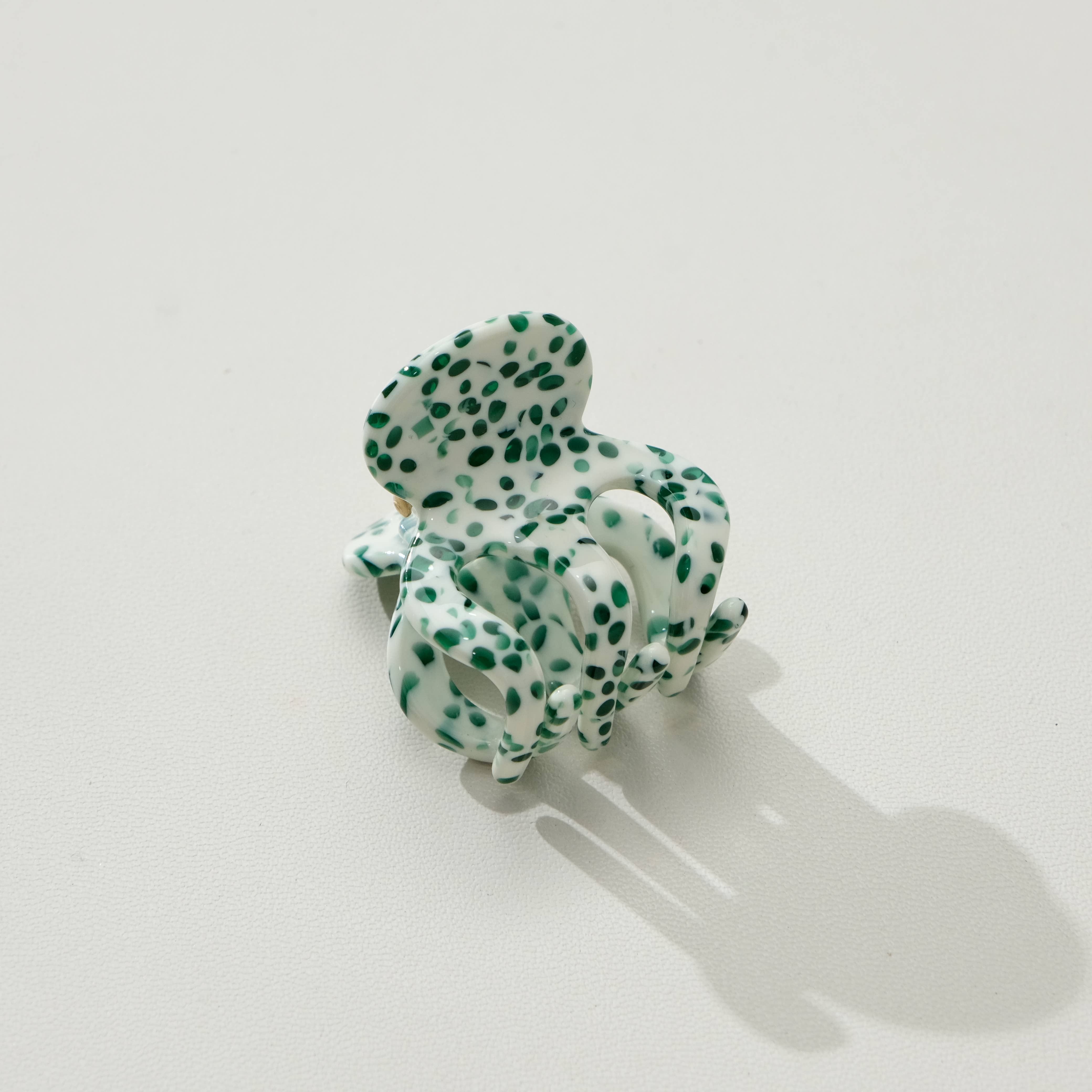 Green and white polka dot hair scrunchie on a light gray background
