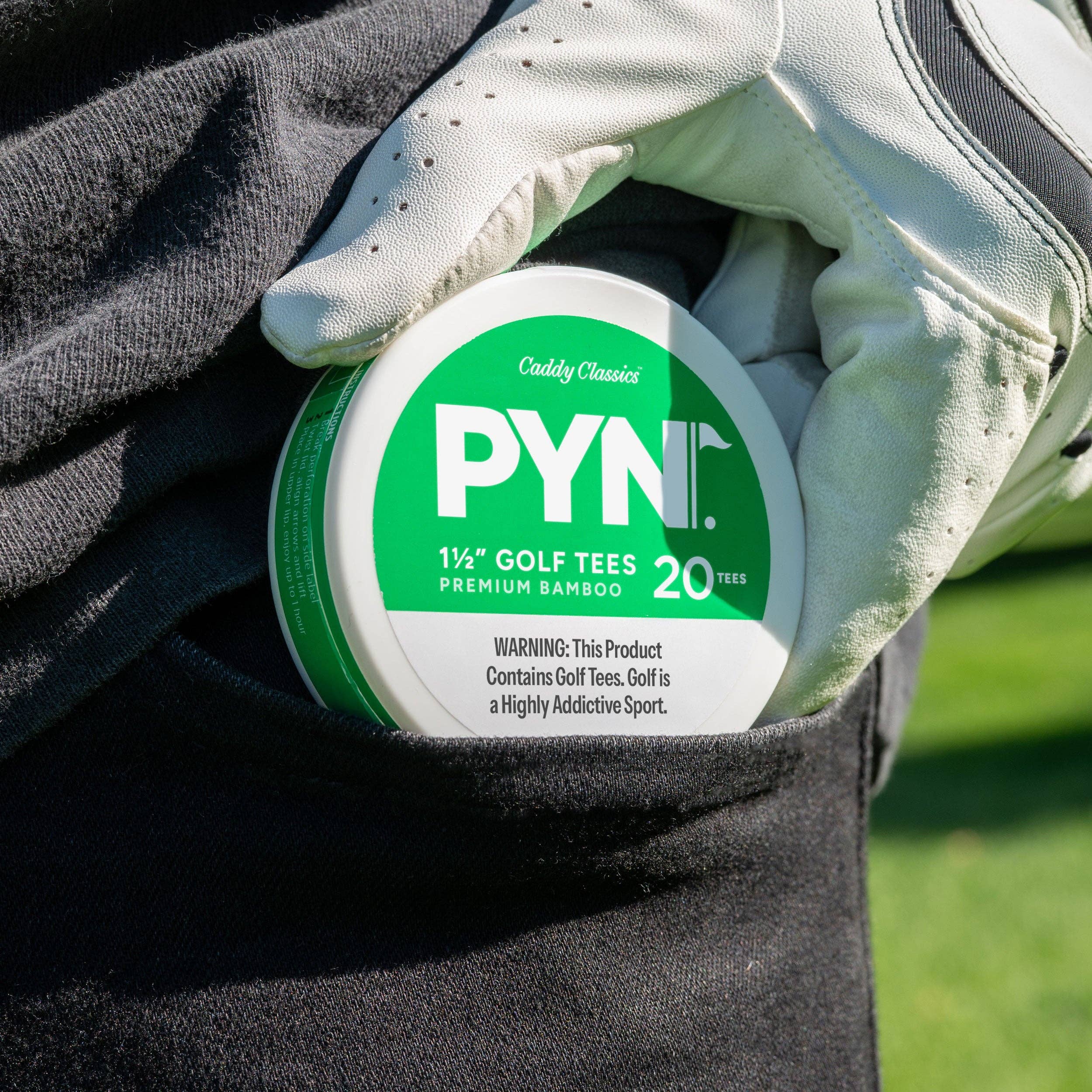 Container of golf tees held by a gloved hand with a grassy background