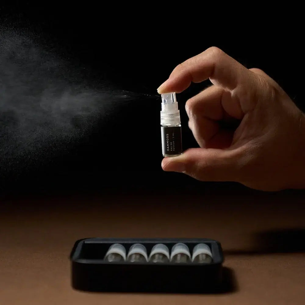 Hand holding a small spray bottle with mist against a dark background