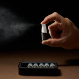 Hand holding a small spray bottle with mist against a dark background