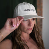 Person wearing a white cap with text, holding it up to their head.