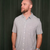 Man wearing a gray striped shirt against a dark curtain background