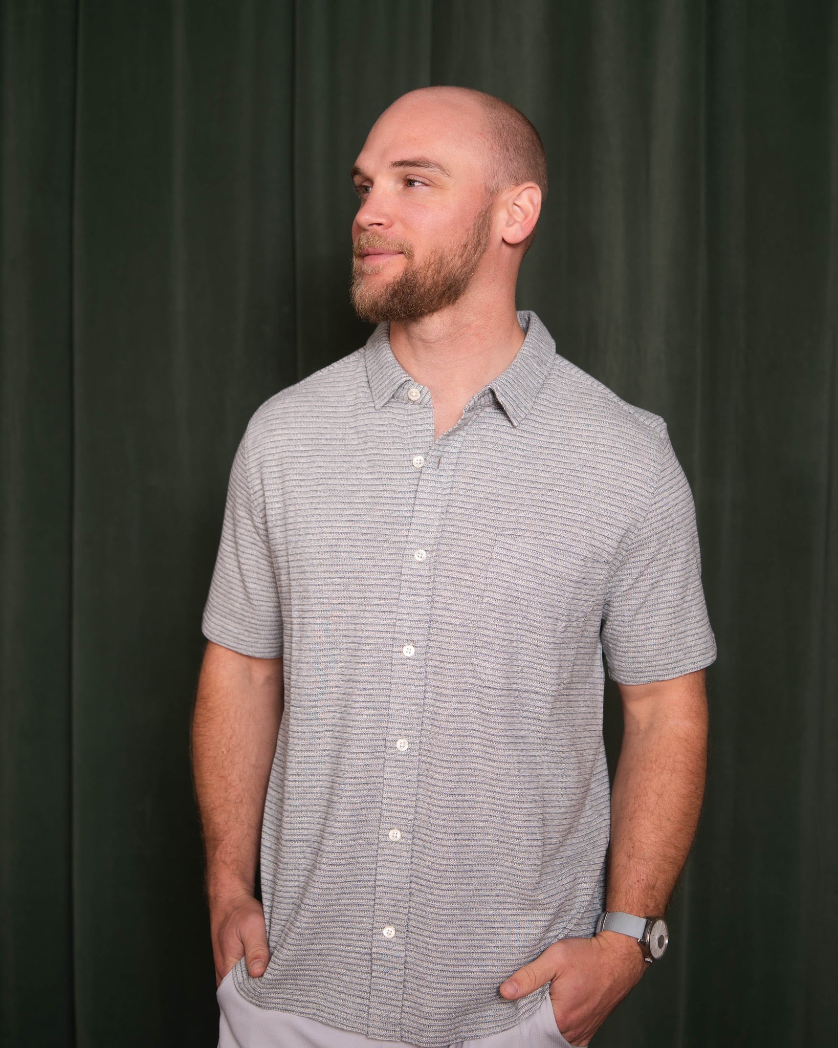 Man wearing a gray striped shirt against a dark curtain background