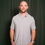Man wearing a gray checkered shirt against a dark green curtain