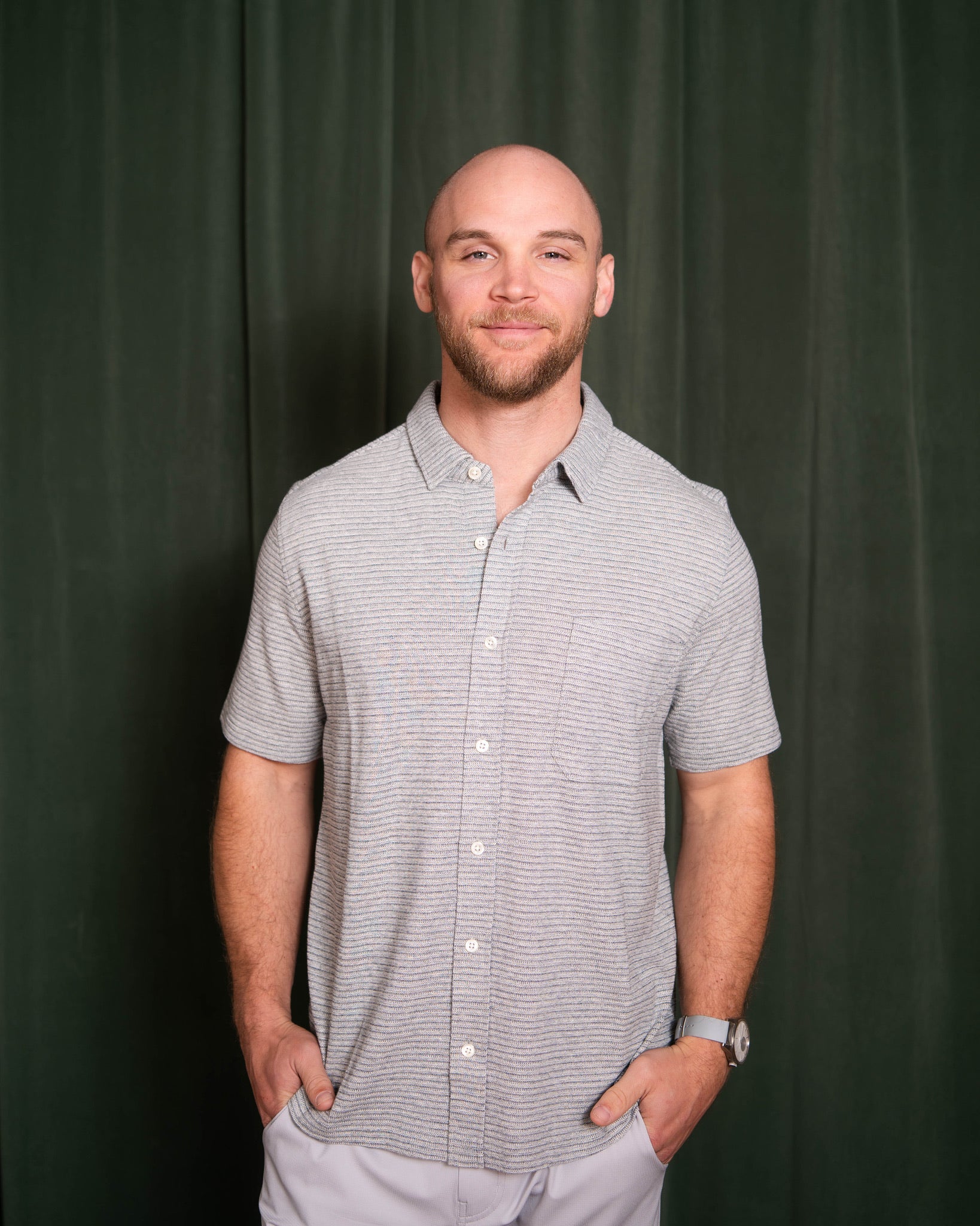 Man wearing a gray checkered shirt against a dark green curtain