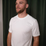 Man wearing a white t-shirt against a dark green curtain background