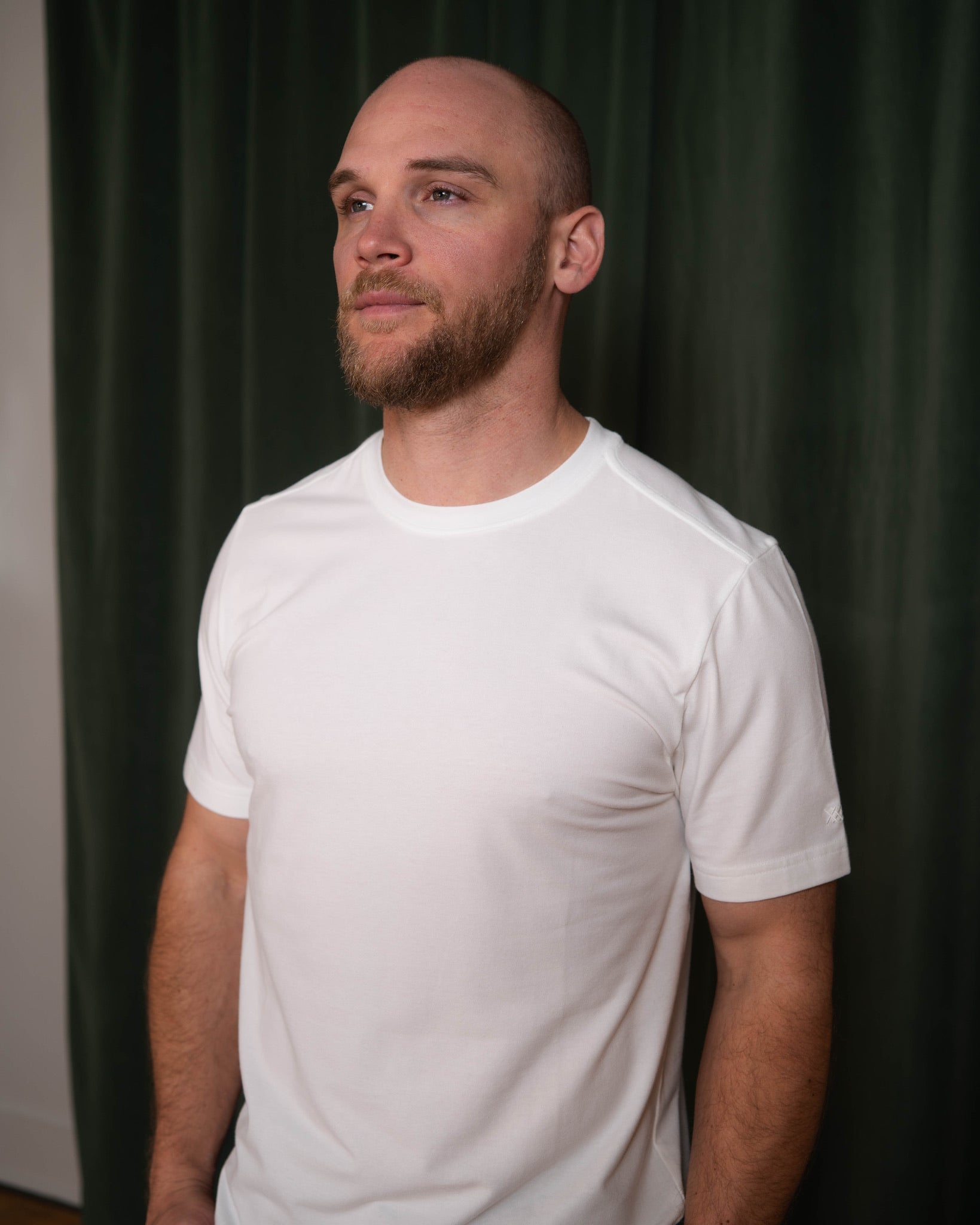Man wearing a white t-shirt against a dark green curtain background