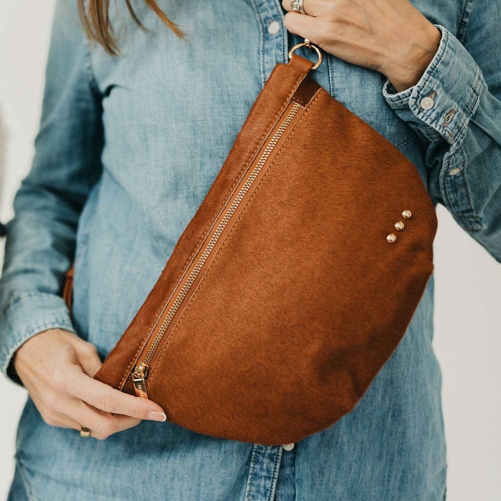 Brown leather bag held by a person wearing a denim jacket.