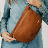 Brown leather bag held by a person wearing a denim jacket.