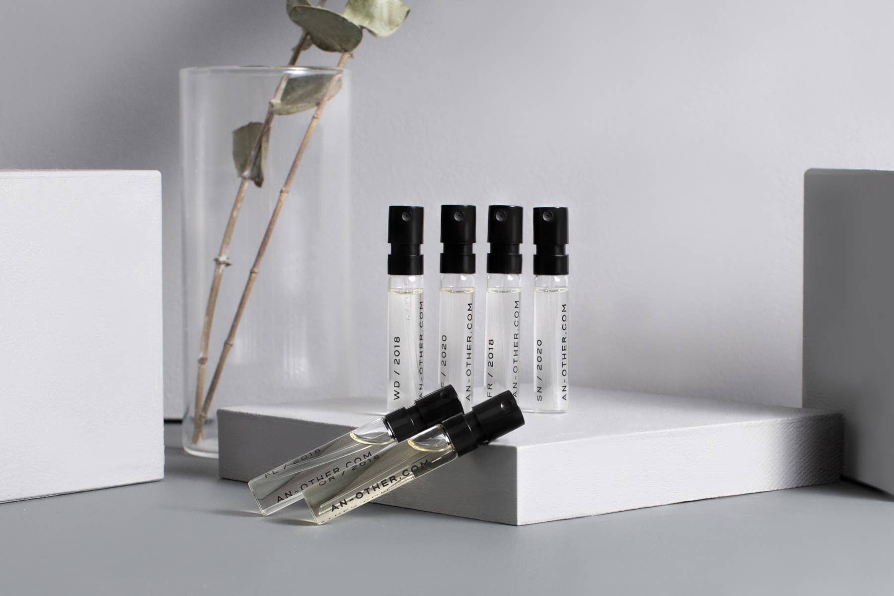 Set of perfume bottles with black caps on a gray surface with a vase and plant in the background