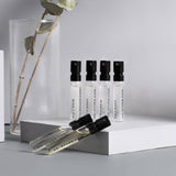 Set of perfume bottles with black caps on a gray surface with a vase and plant in the background