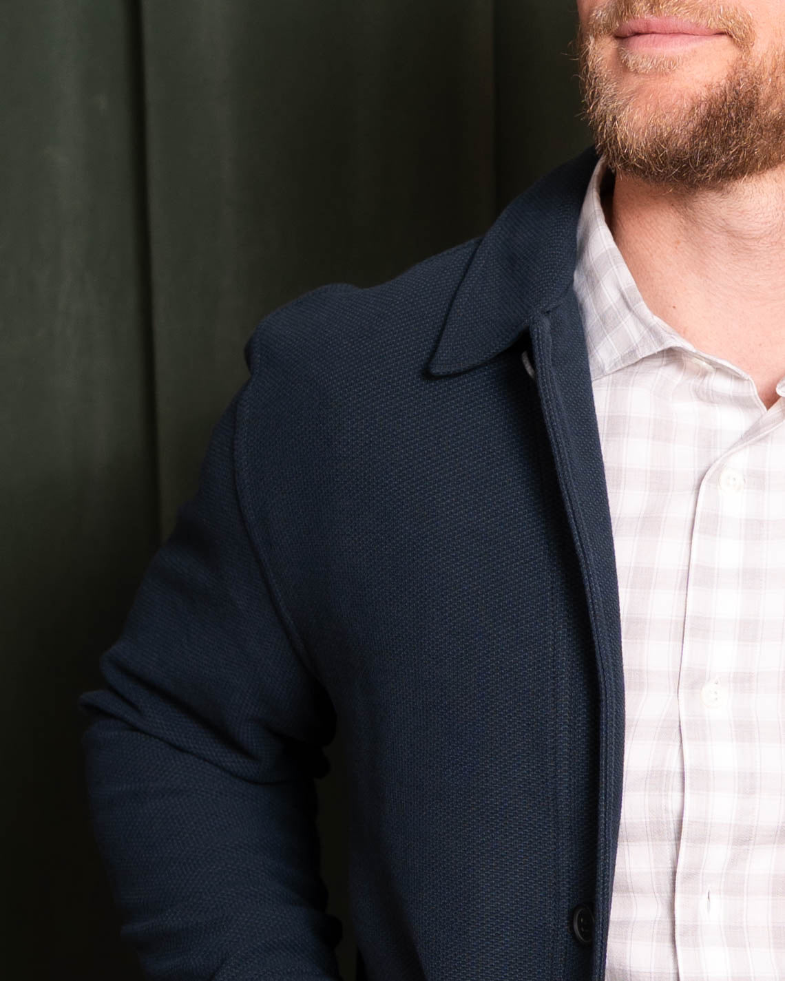 Man wearing a dark blue coat over a light-colored shirt against a dark background