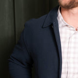 Man wearing a dark blue coat over a light-colored shirt against a dark background