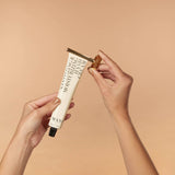Hand holding a tube of hand cream on a beige background
