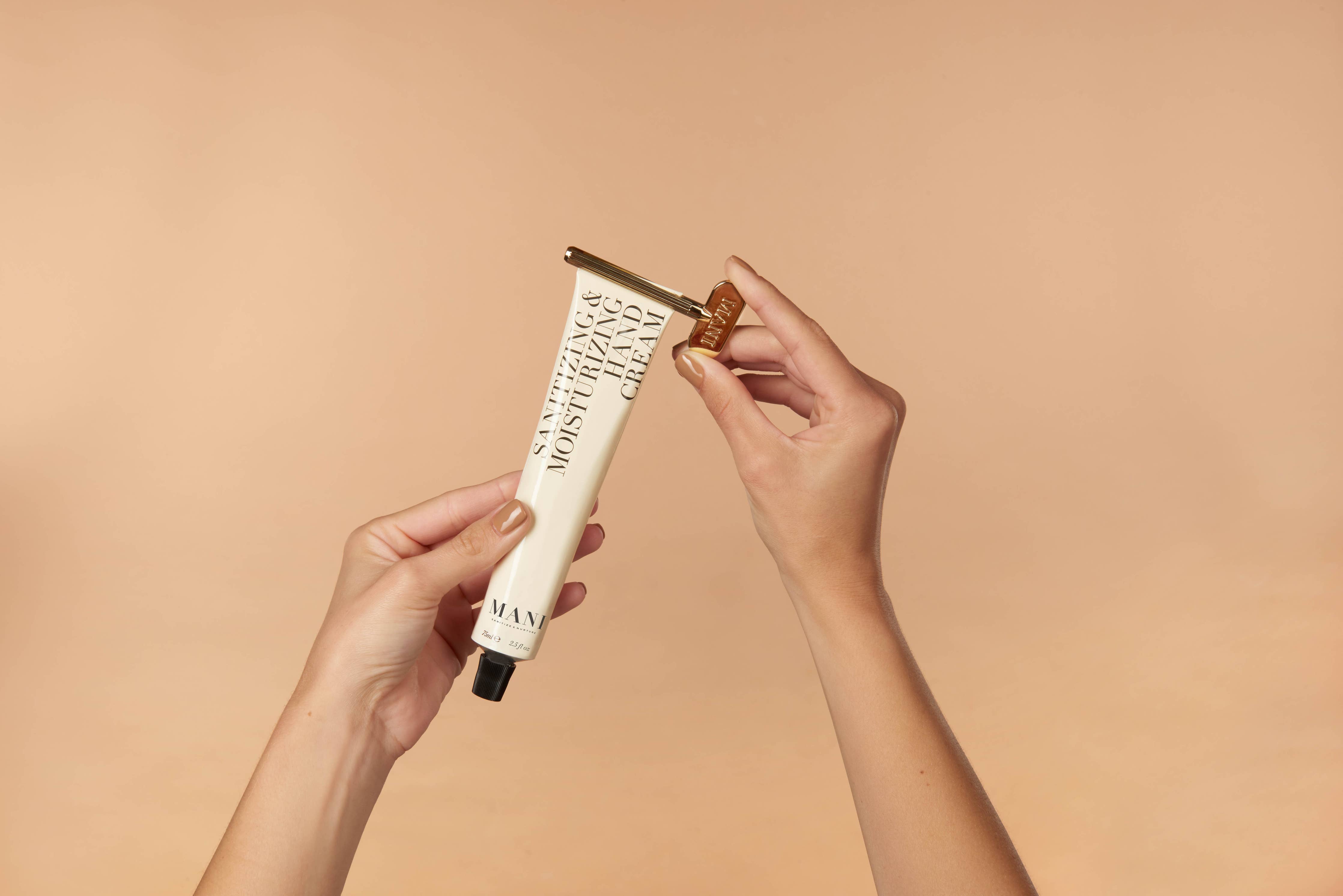 Hand holding a tube of hand cream on a beige background