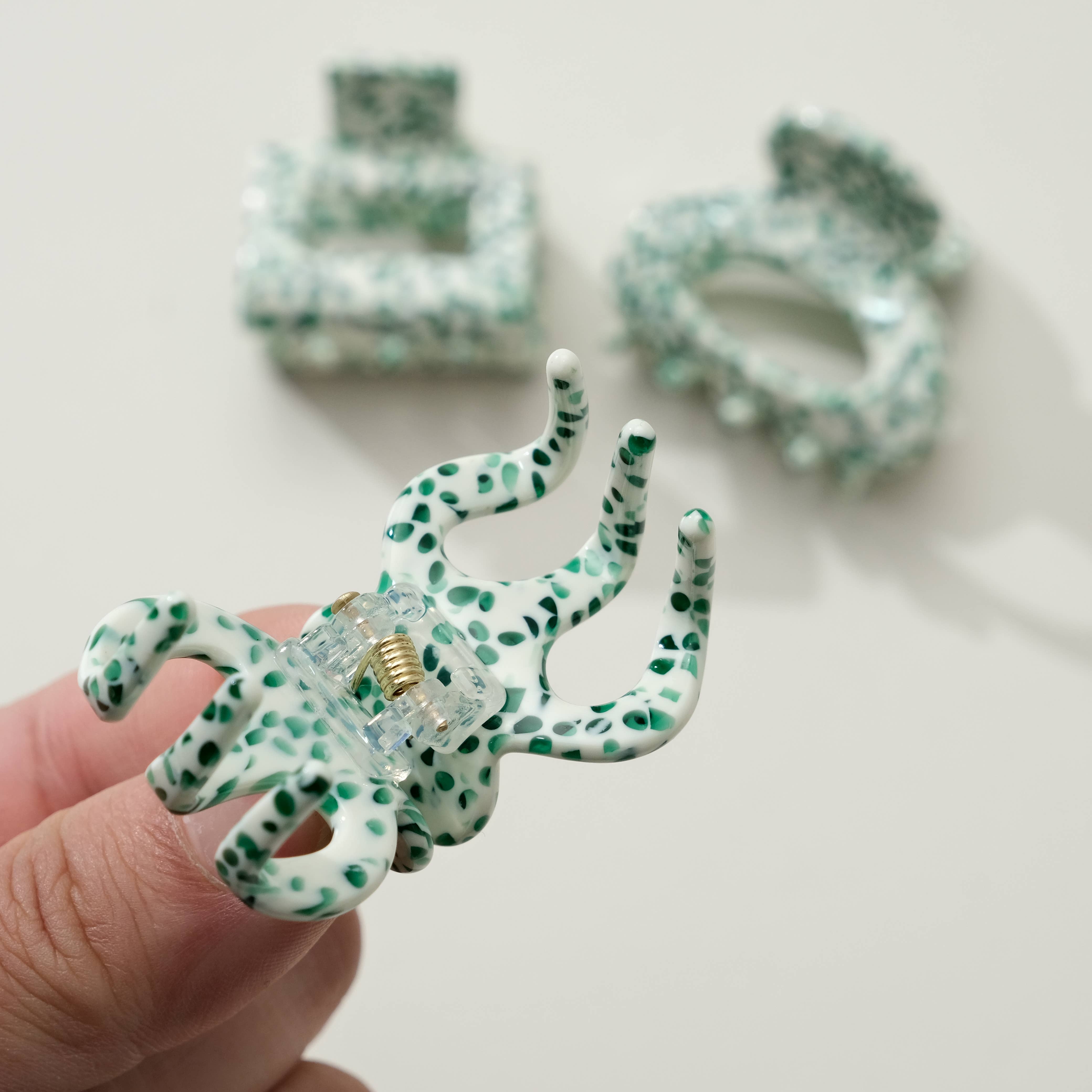 Green and white polka dot hair tie held by a hand with more hair ties in the background.
