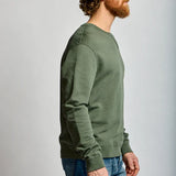 Man wearing a green sweater and blue jeans against a plain background