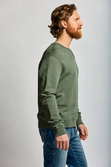 Man wearing a green sweater and blue jeans against a plain background