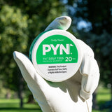 Hand holding a container of PYN golf tees with a blurred green outdoor background