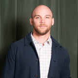Man wearing a dark coat over a light shirt against a green curtain background