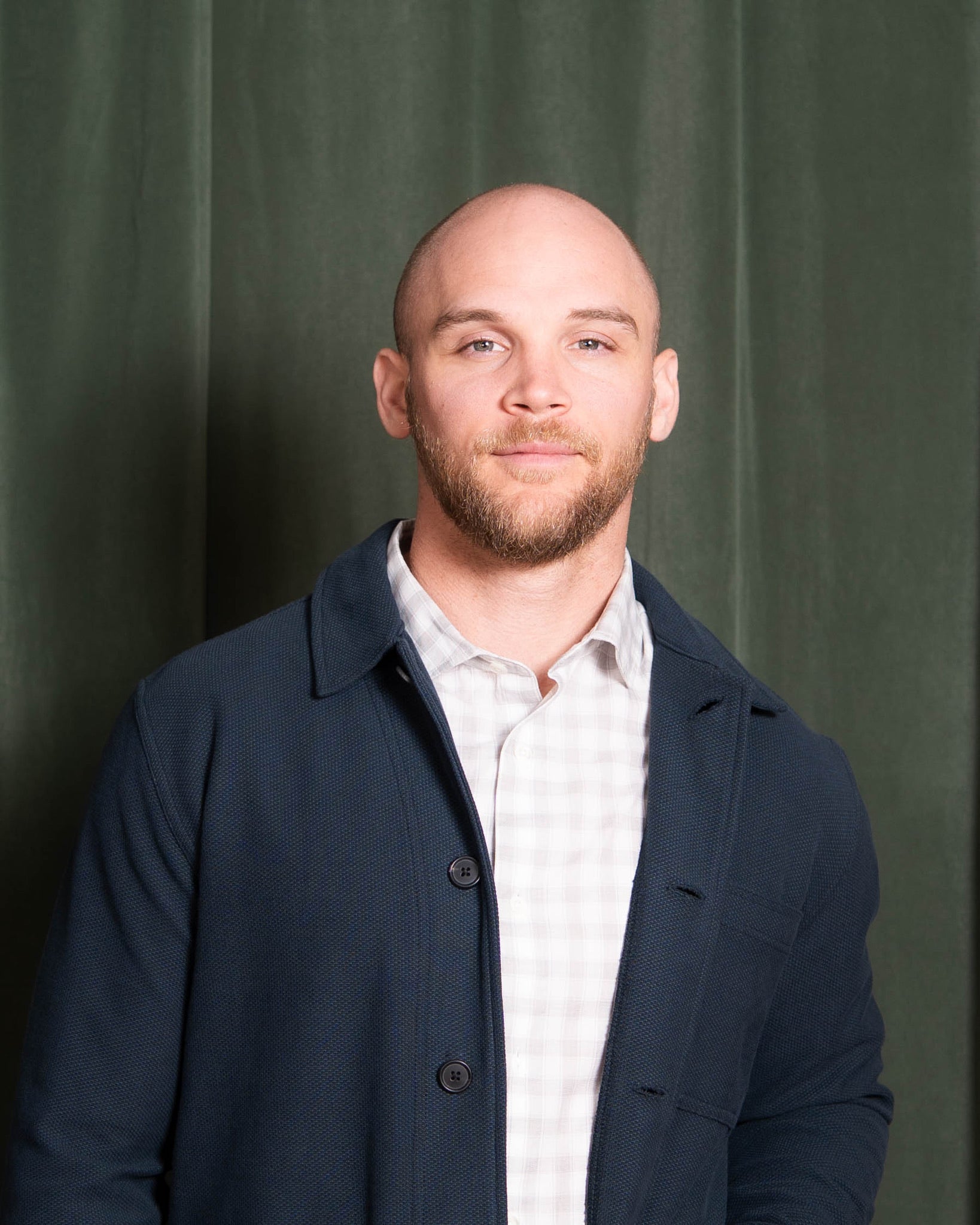 Man wearing a dark coat over a light shirt against a green curtain background