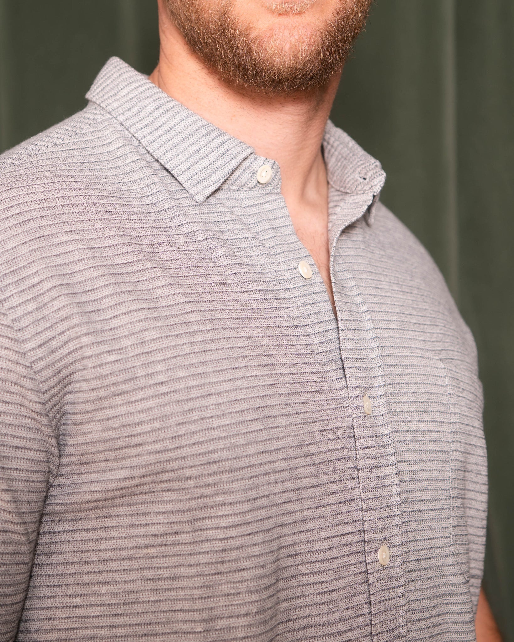 Close-up of a person wearing a gray striped shirt against a green background