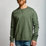 Man wearing a green sweatshirt and blue jeans against a gray background