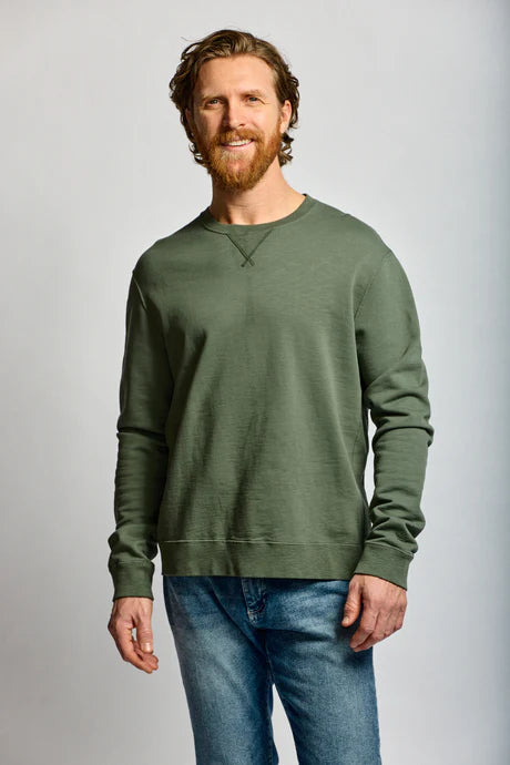 Man wearing a green sweatshirt and blue jeans against a gray background