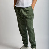 Person wearing green jogger pants and white sneakers on a plain background