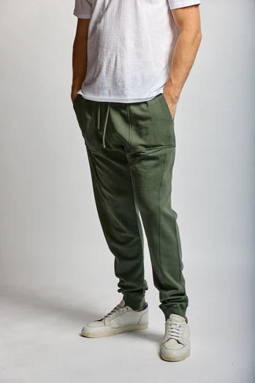 Person wearing green jogger pants and white sneakers on a plain background
