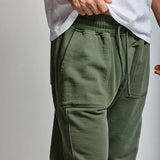 Person wearing green sweatpants and a white shirt on a plain background