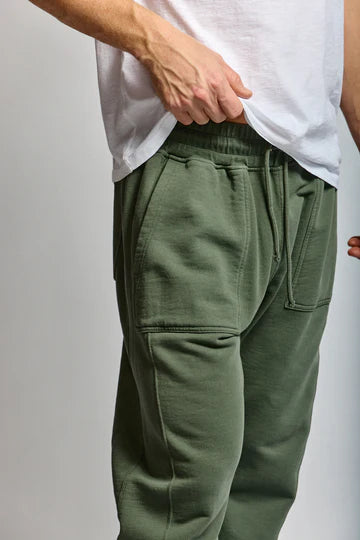 Person wearing green sweatpants and a white shirt on a plain background