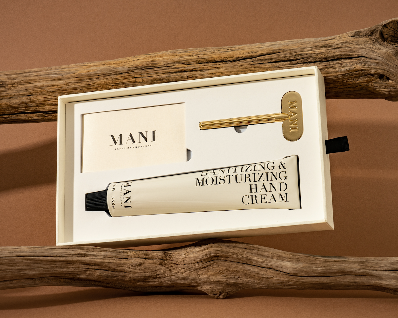 Mani sanitizing and moisturizing hand cream in a box with a gold applicator on a brown background.