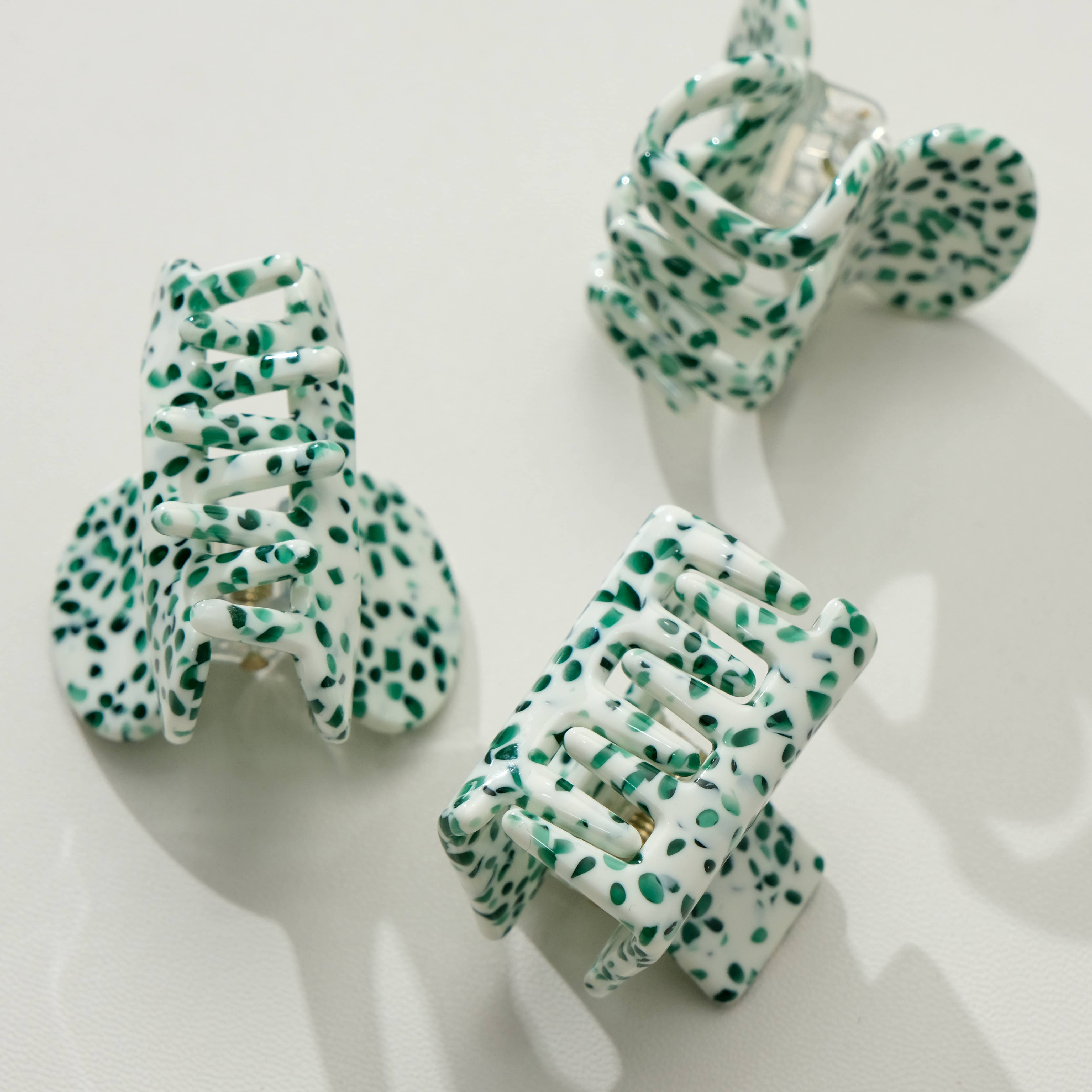 Three green and white polka dot hair clips on a white background