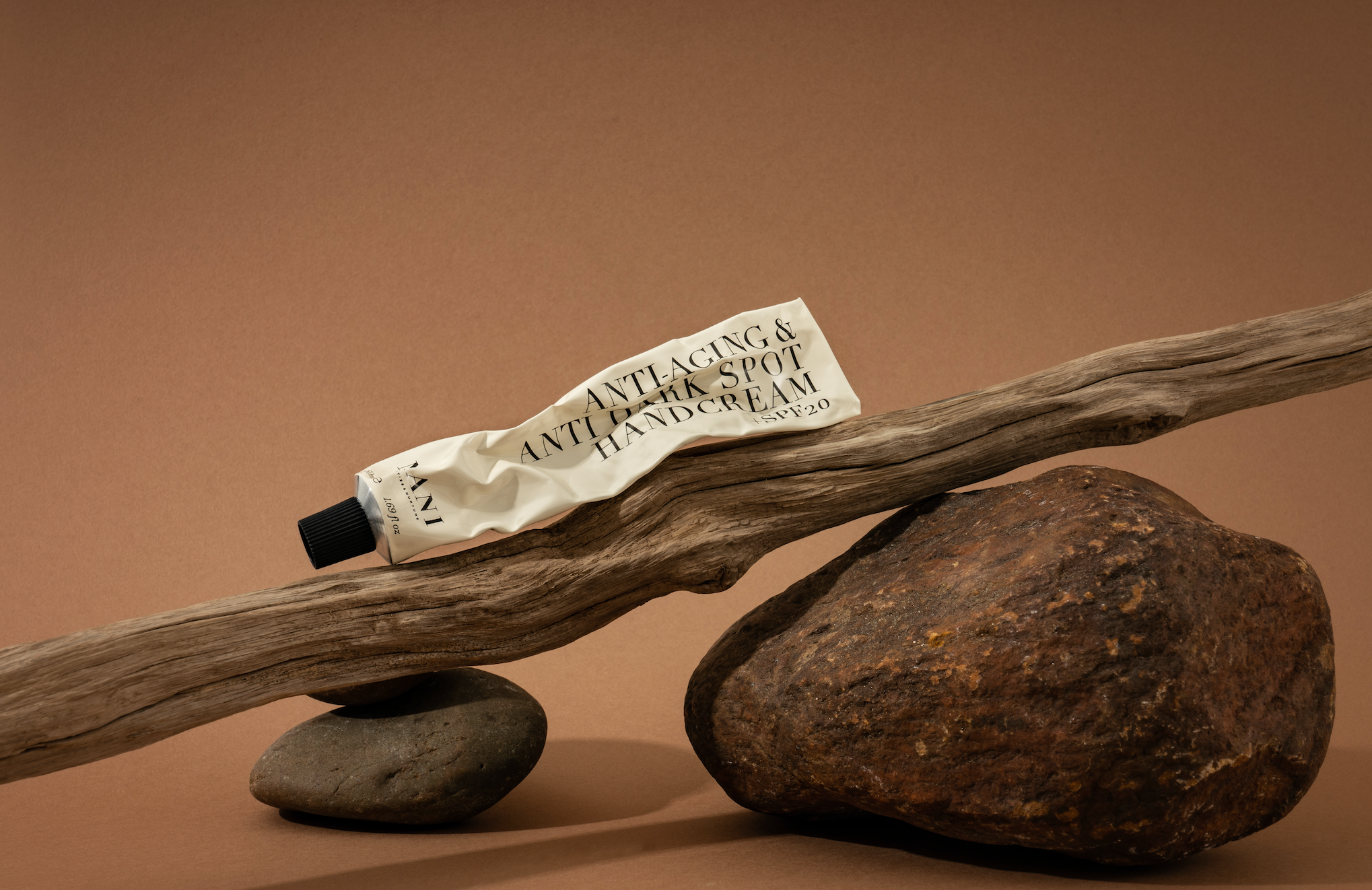 Tube of hand cream on a wooden stick with rocks on a brown background