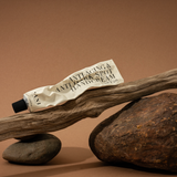 Tube of hand cream on a wooden stick with rocks on a brown background
